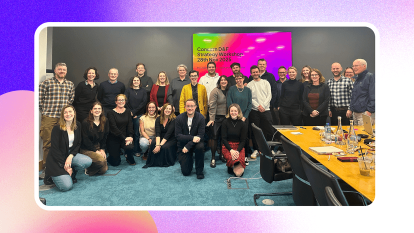 A group of people stand together in an office meeting room with a screen behind them that says 'Concern Worldwide D&F Strategy workshop'