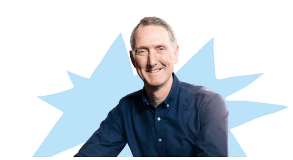 Björn Conway, TPXimpact CEO, smiling in front of a white background with a pastel-blue "kapow"-style shape on it. (manifesto is part of TPXimpact).